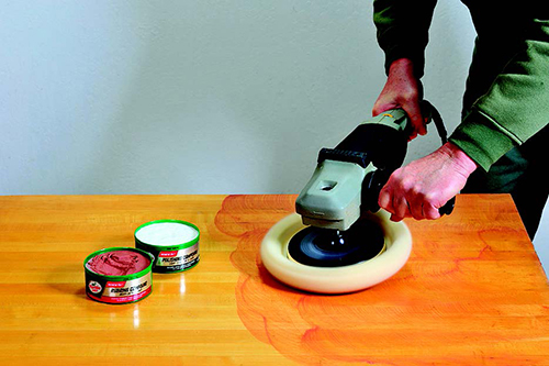 Start buffing with coarse red rubbing compound, then finer white polishing compound. Before switching grits, clean all rubbing compound from the wood surface and the buff head.