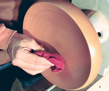 The author applies his liquid friction polish to a spinning maple bowl. As the friction spreads and polishes the product, a smooth, shiny finish begins to appear.