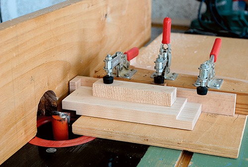 Most of the ends of the train car bases will need to be rabbeted to form the hitch connections later. Since these workpieces are small, use caution when milling them at the router table. A sliding jig with hold-down clamps can help secure each part for safer routing close to the bit.