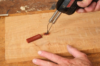 Using an electric iron to apply burn-in stick to a void.