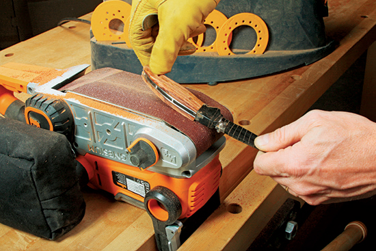 Continue to shape and smooth the handle. Hold the knife against a clamped belt sander near the front wheel so the belt spins away from you.
