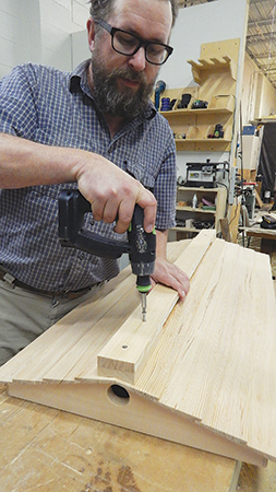 Fasten the ridge cap to the roof ends with pairs of countersunk screws only — no glue. That way, you can remove it if the ridge vent screen ever needs to be cleaned or replaced.