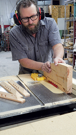 To create the long beveled edges on the top bars, the author used a special push block that fits around the top bar blanks and holds their lapped ends down against the saw table. It has a cutout area in the middle to accommodate the taller part of the upturned bars. Two cuts, with the saw blade tipped to 551⁄2° and passing through a zero-clearance throatplate, did the job.