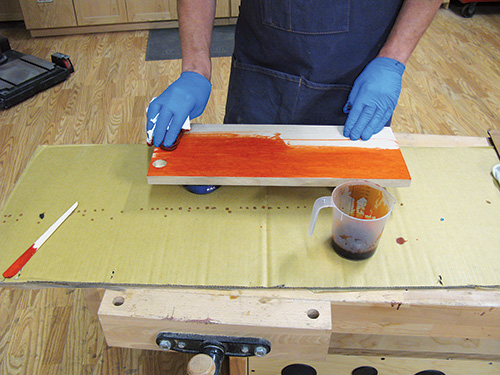 Spreading an orange dye base over veneered panels