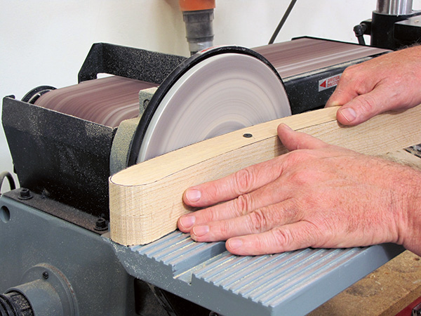 Sanding chair parts smooth with disc sander