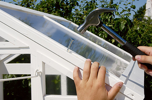 Hammering bolts into place on fold-up greenhouse roof