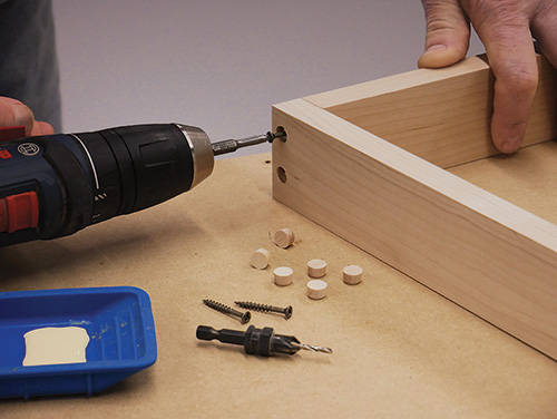 Screwing leg components into modern coffee table base with wood plugs to hide the screw holes