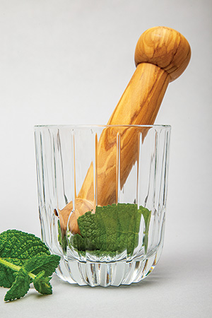 Mint leaves being crushed with an olivewood pestle