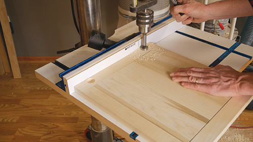 Using drill press to cut hinge holes into cabinet door
