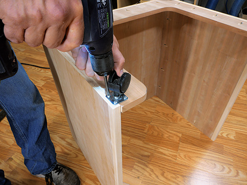 Screwing casters in place on sewing cabinet