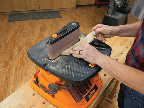 Finish sanding coat hook on belt sander