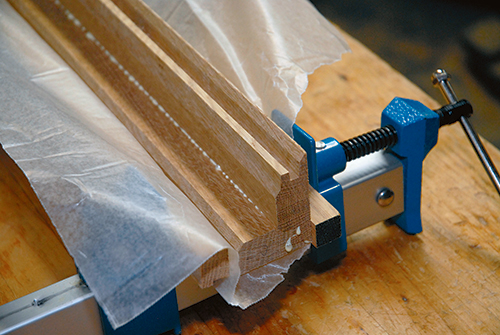 Begin leg assembly by gluing two sides together to form leg halves. The author lined his clamps with scrap blocks to prevent the sharp mitered edges from being damaged by clamp pressure.