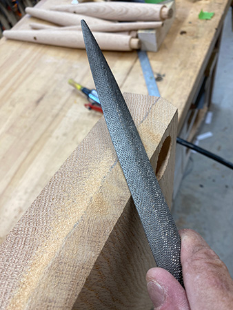 Smoothing sharp edges of stool with hand rasp