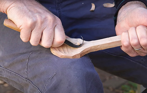 Carving scoop portion of spoon with a hook knife