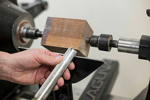 Square blank on lathe with a chisel held next to it