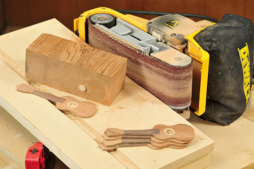 A jig made from scrap wood and a 1/2"-dia. dowel allows you to safely belt sand the thin ornaments.