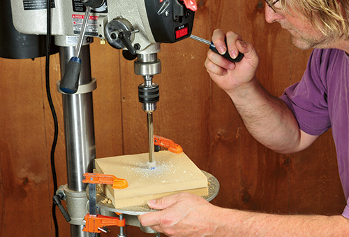 After drilling a 3/16" pilot hole concentrically through the dowel, a 15/32" bit is used to enlarge the hole to full size. Feeding the bit slowly and only drilling a little at a time keeps the dowel from spinning.