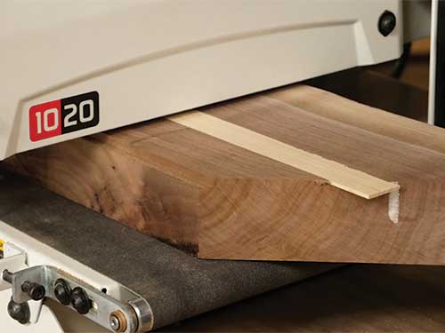Sanding down inlay strip in walnut tabletop with drum sander
