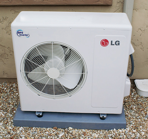 The compressor-condenser unit for a mini-split heat pump system is designed to be mounted out-of-doors and wired to a 240-volt electric circuit. Tubing carries heat or cold to an evaporator unit inside the shop.